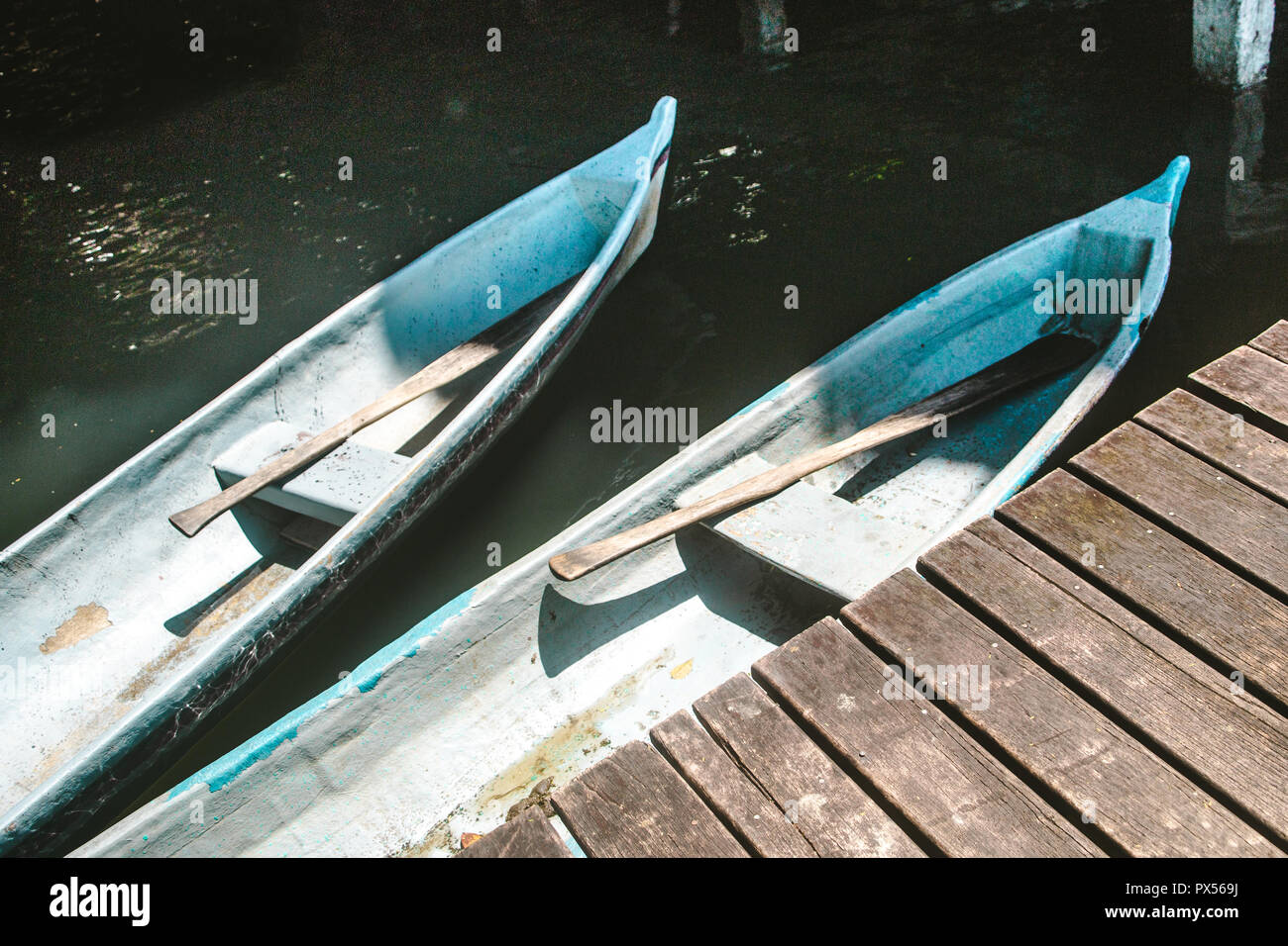 Two canoes with wooden oars docked by a jetty on a lake Stock Photo