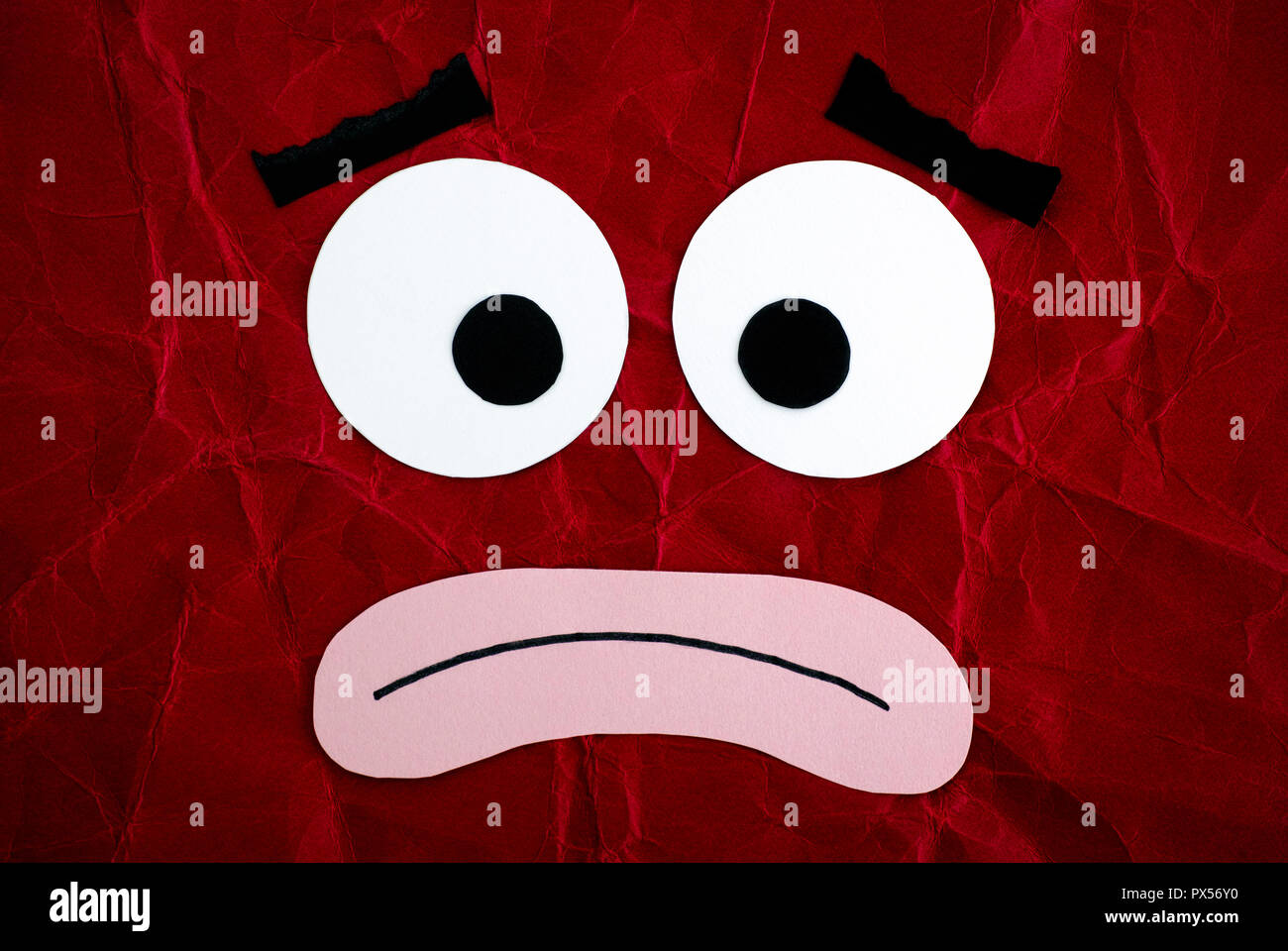 Sad character. Emotional face made from paper. Red background. Stock Photo