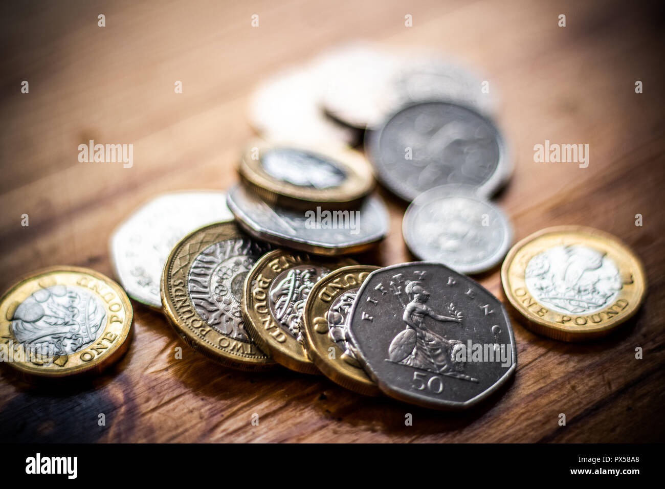 New Great British Pound GBP Coins laying casually on wooden surface. Wealth, Money, Cash, Change. Stock Photo