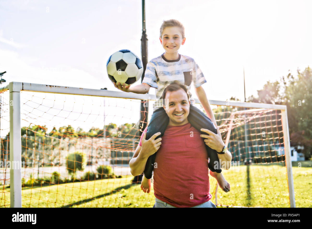 man with child playing football outside on field Stock Photo