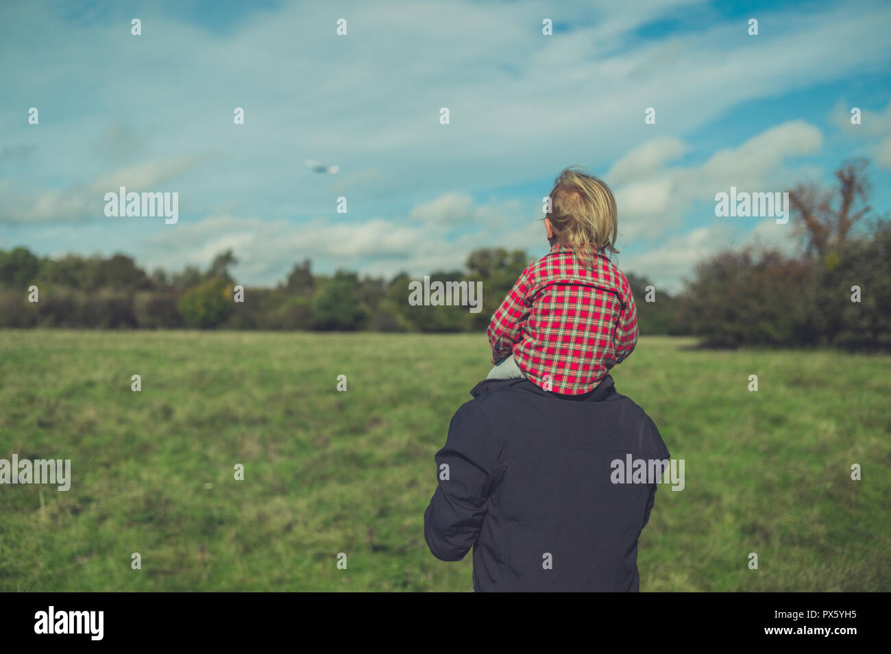 A little toddler is riding on his fathers shoulders in nature Stock Photo