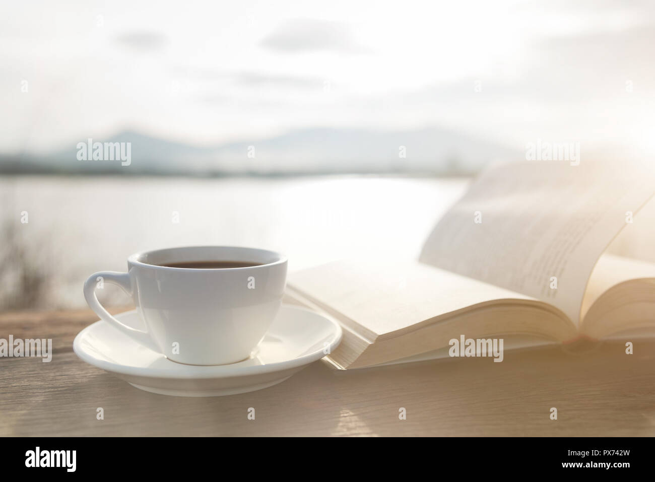 Cup of coffee and book on a wooden table in morning sunlight with a ...