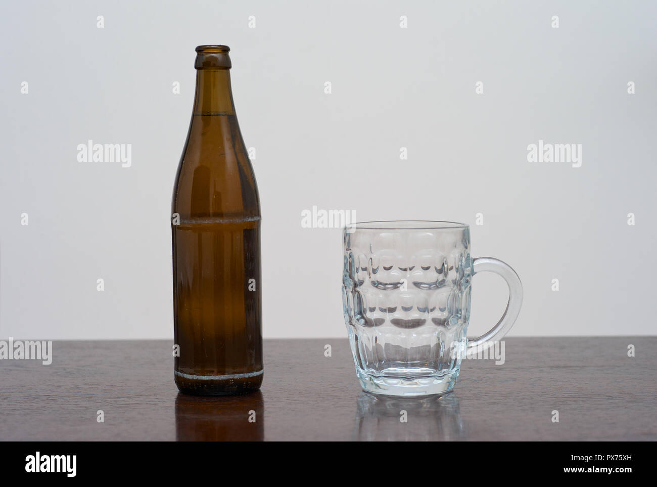 Empty Dimpled Pint Glass and a Bottle of Beer on a Brown Wooden Table Stock Photo