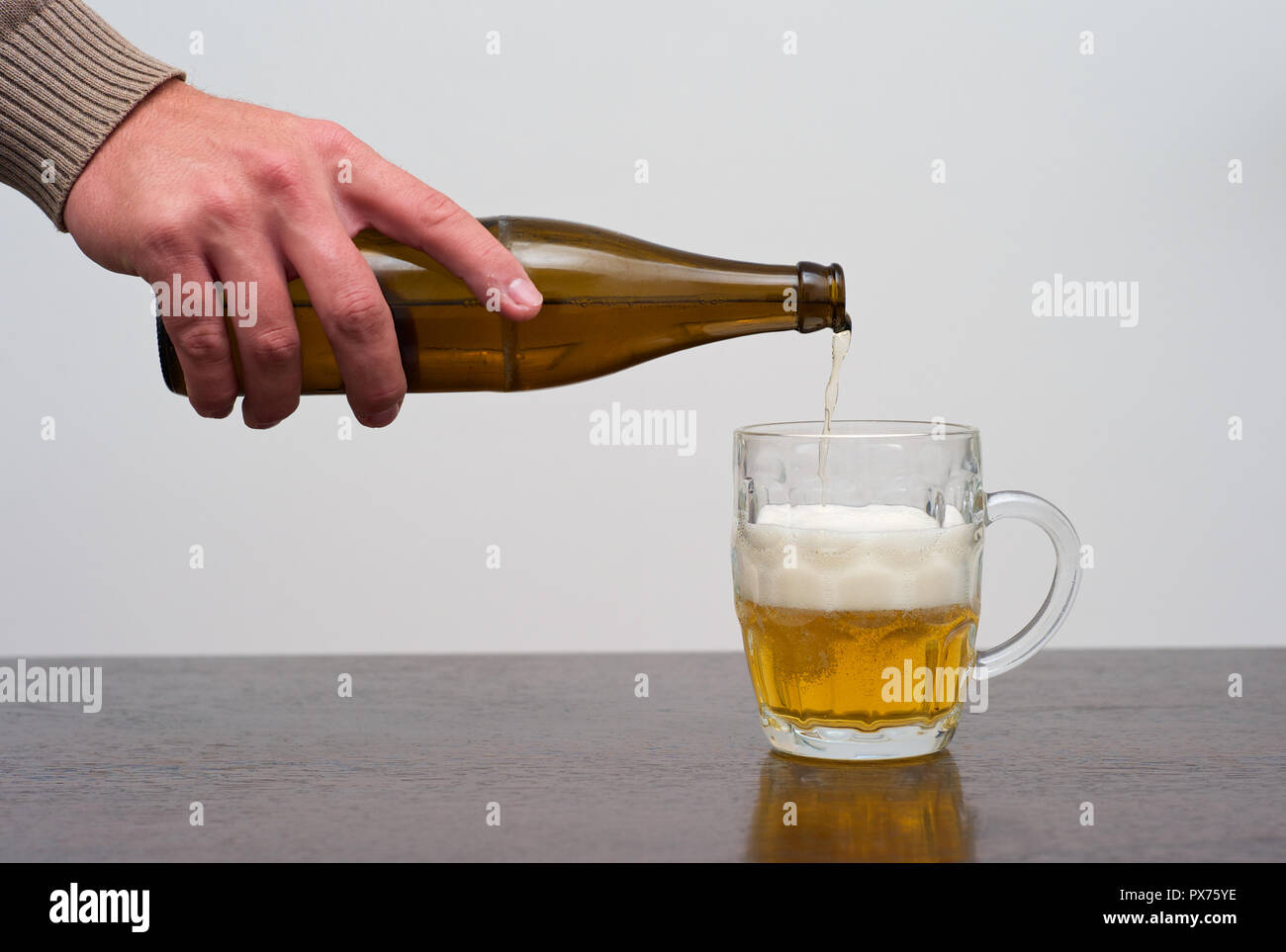 Filling a Dimpled Pint Glass of Beer from the Bottle, Hand Pouring Ale in a Tankard Stock Photo