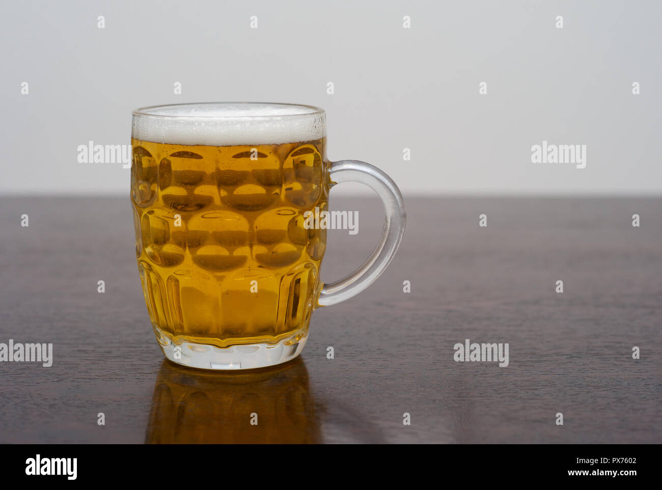 Pint of Beer in a Dimpled Pint Glass on a Dark Wooden Table, a Tankard of Blonde Lager or Pilsner Stock Photo