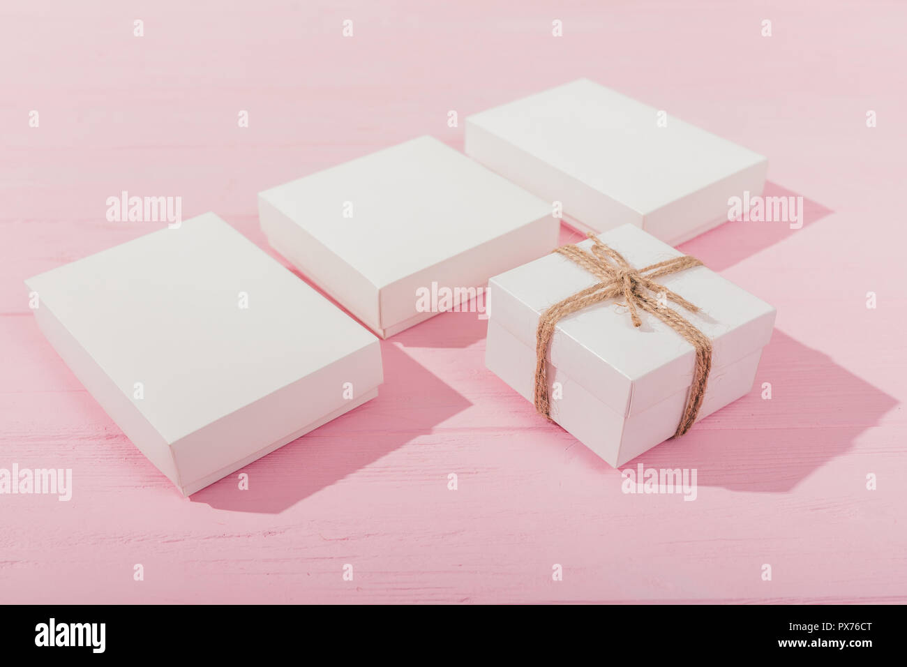 Close-up gift boxes on pink wooden table. Set of white presents for celebration. Stock Photo