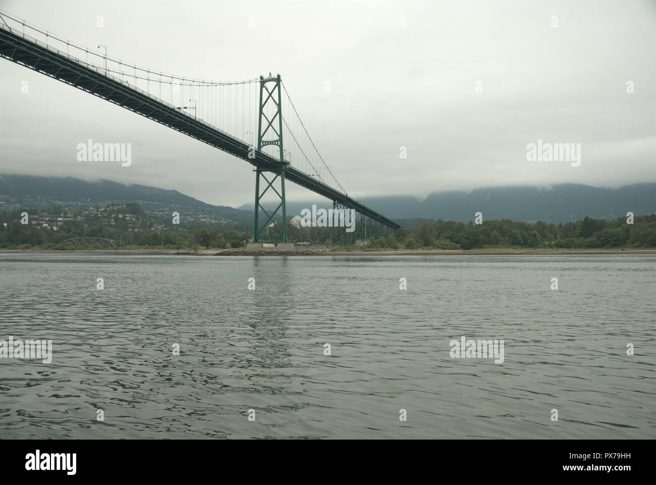 Under gray cloudy skies, the Lions Gate Bridge spans Burrard Inlet from Stanley Park in Vancouver to North Vancouver, British Columbia, Canada Stock Photo