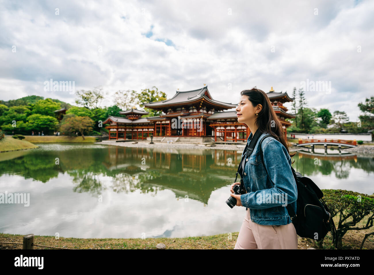 elegant female traveler walking around the pond to the temple in the background. Kyoto travel tourist woman on vacation. Byodo in located beside the g Stock Photo