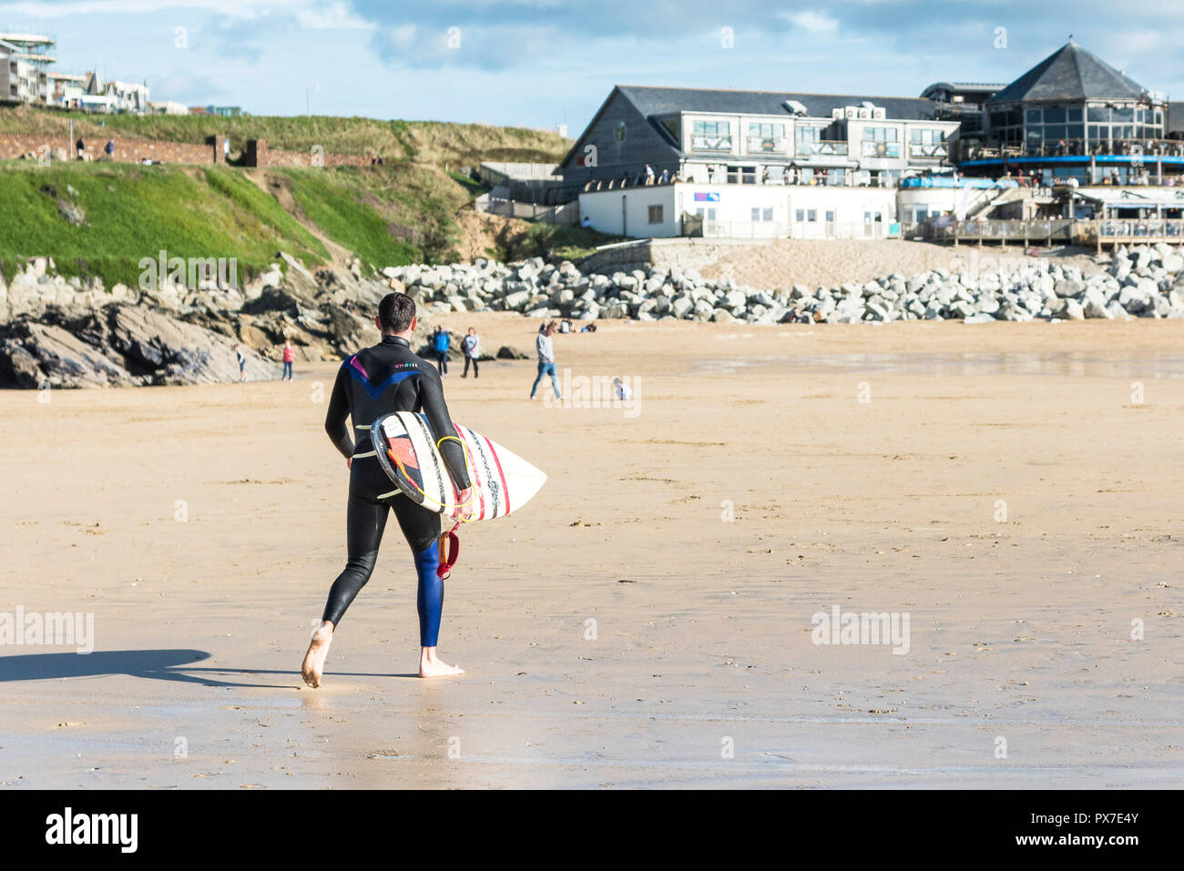A surfer carrying his surfboard walking on Fistral Beach in Newquay in Cornwall. Stock Photo