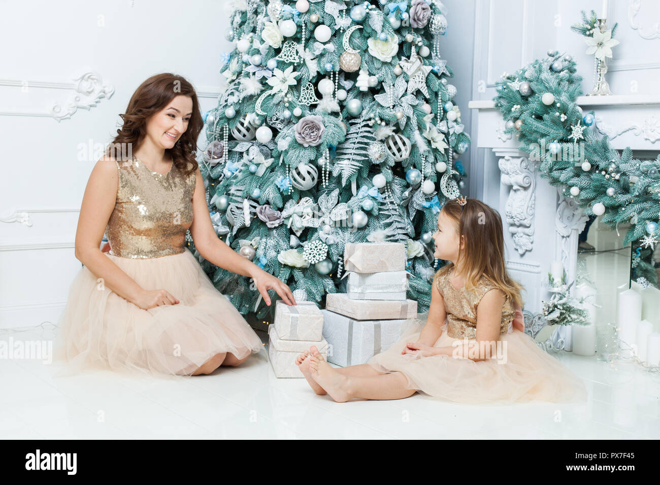 Mom and daughter sitting under the Christmas tree near the boxes with gifts. Stock Photo