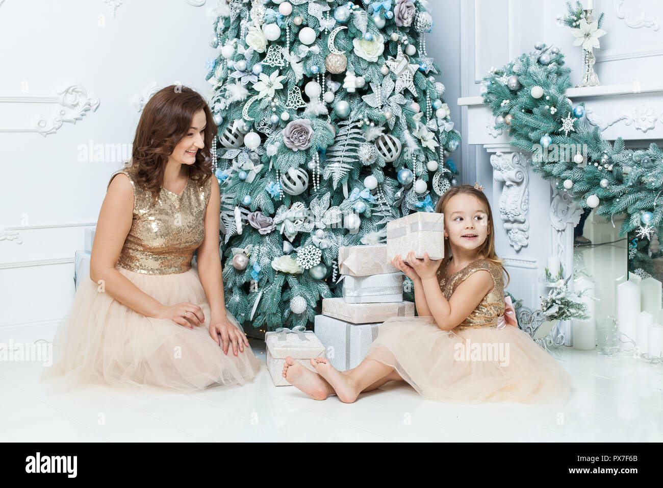 Happy mom and daughter near the Christmas tree. Girl holding a box with a gift. Stock Photo