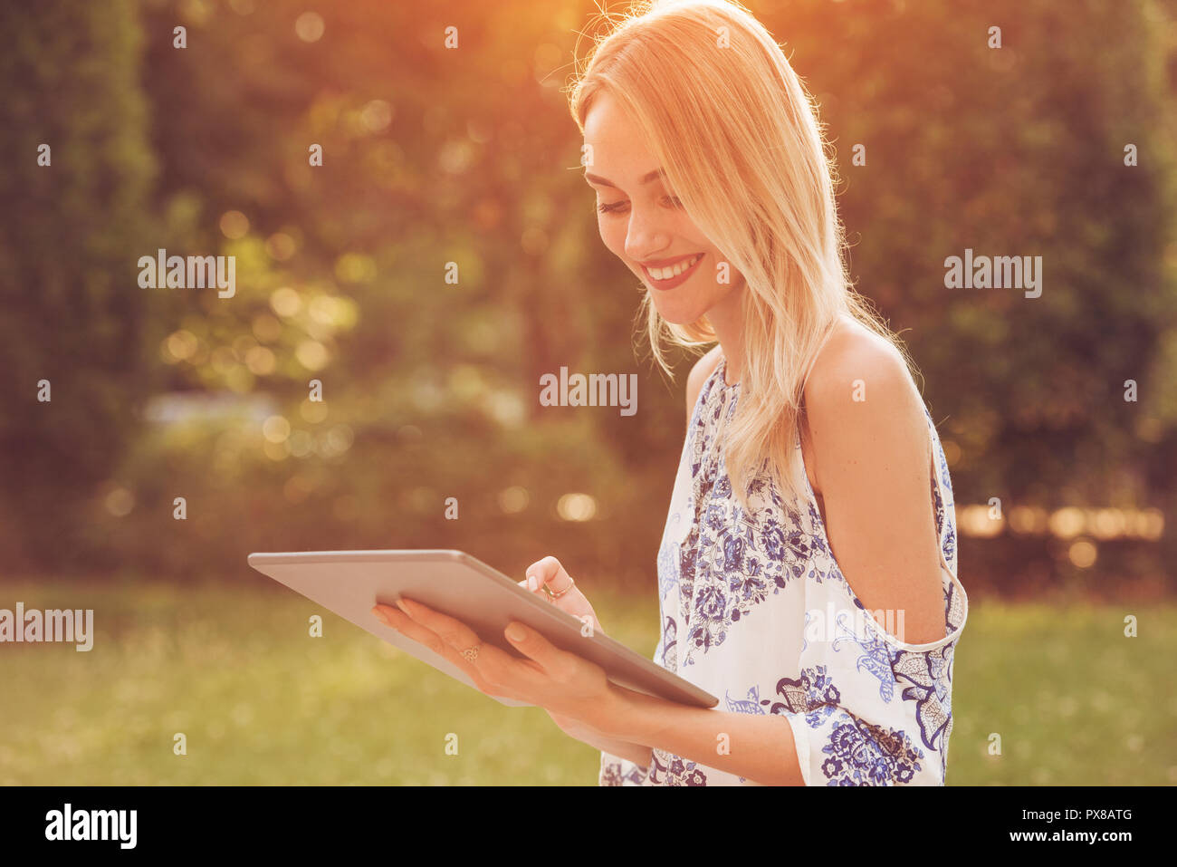 Beautiful Young Woman is using an app in her tablet pc device to read email, receive text, write a message or browse the internet while outdoors Stock Photo