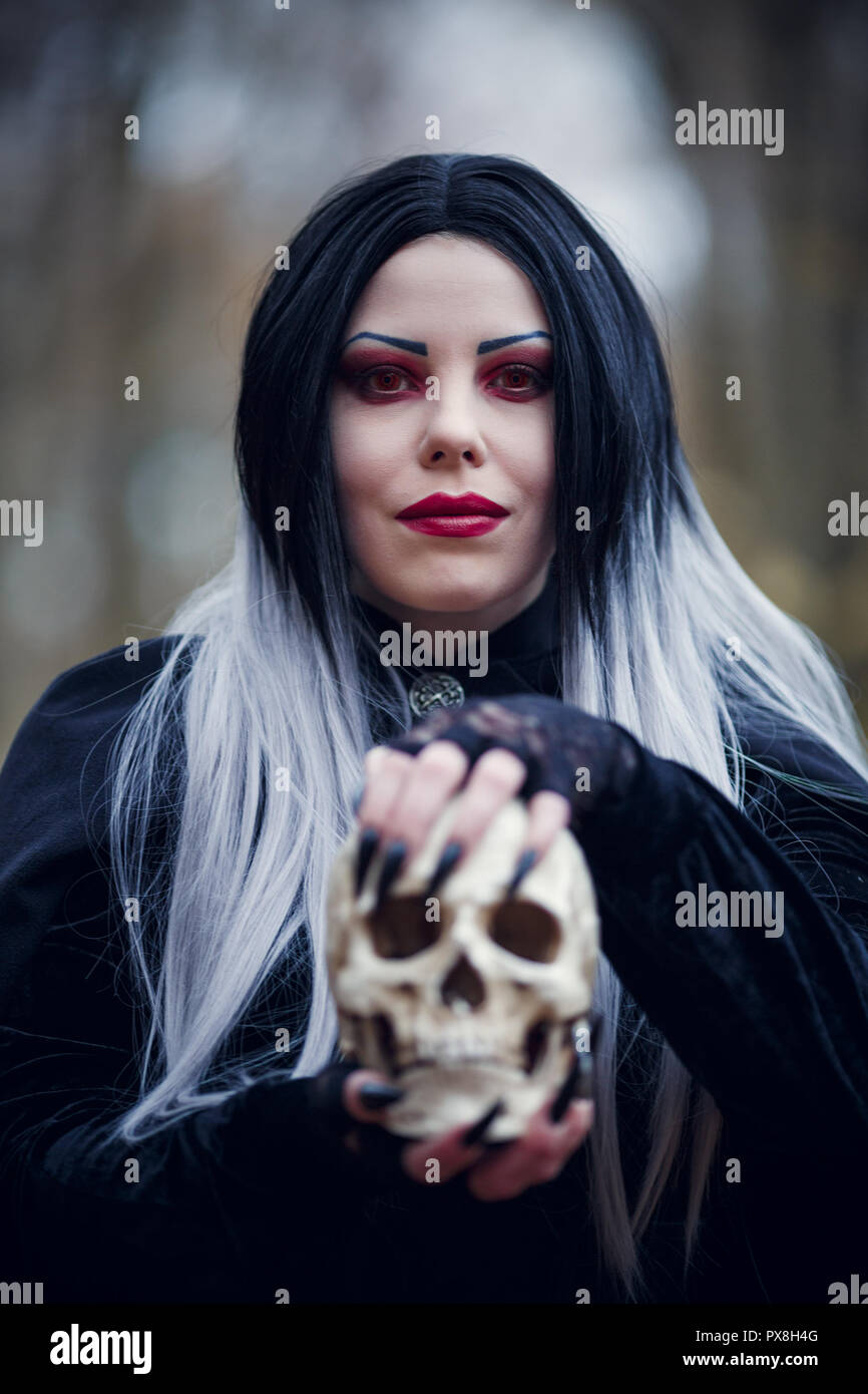 Portrait of witch woman in black cloak with skull Stock Photo - Alamy