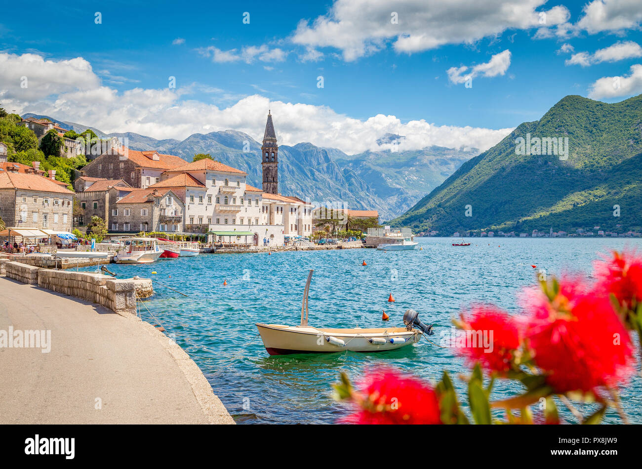 Scenic panorama view of the historic town of Perast at famous Bay of Kotor with blooming flowers on a beautiful sunny day with blue sky and clouds in  Stock Photo