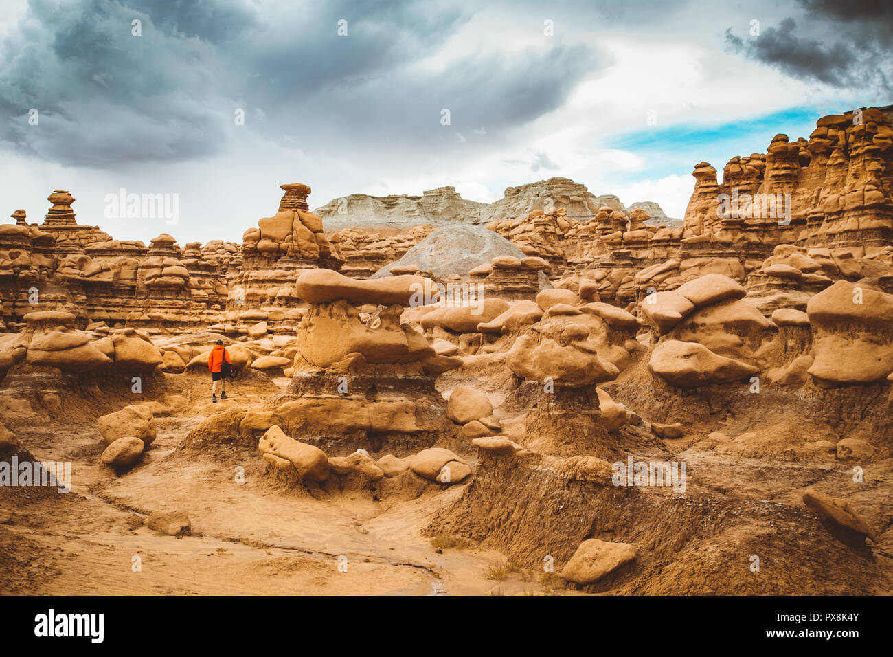 Panoramic view of hiker in red jacket standing in Goblin Valley State Park amidst beautiful hoodoos sandstone formations, Utah, USA Stock Photo