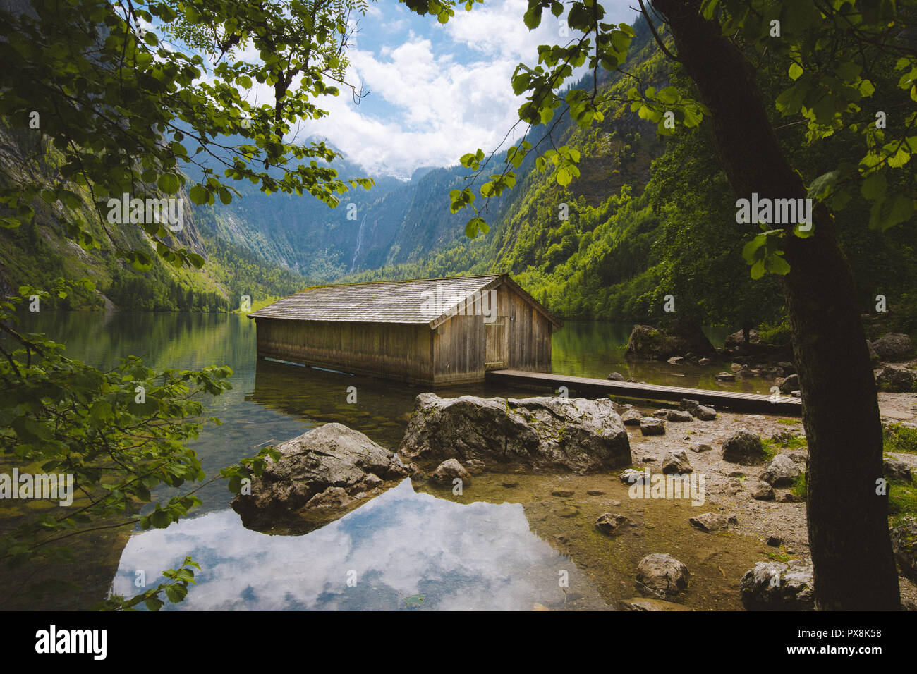 Panoramic view traditional old wooden boat house at scenic Lake Obersee on a beautiful day with blue sky and clouds in summer, Bavaria, Germany Stock Photo