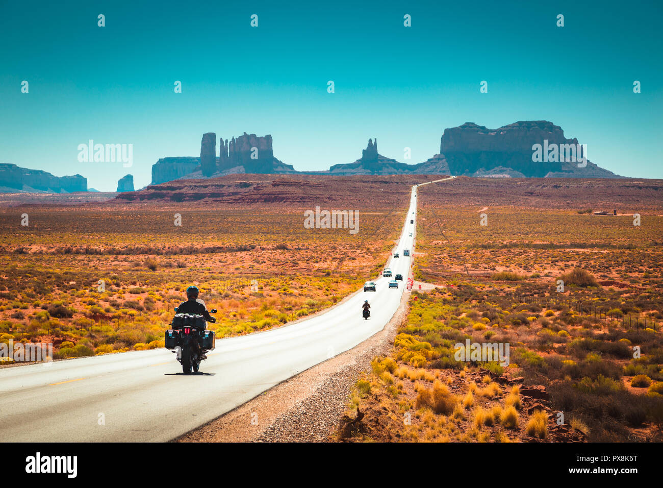 Classic panorama view of motorcyclist on historic U.S. Route 163 running through famous Monument Valley in beautiful golden evening light at sunset in Stock Photo