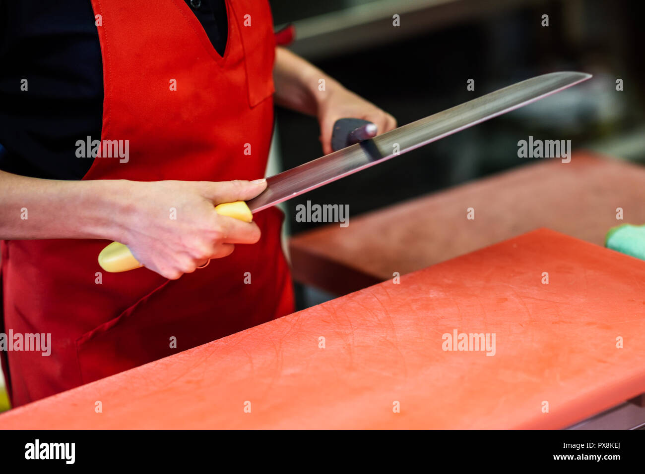 Young female butcher sharpening a knife in a butcher shop Stock Photo