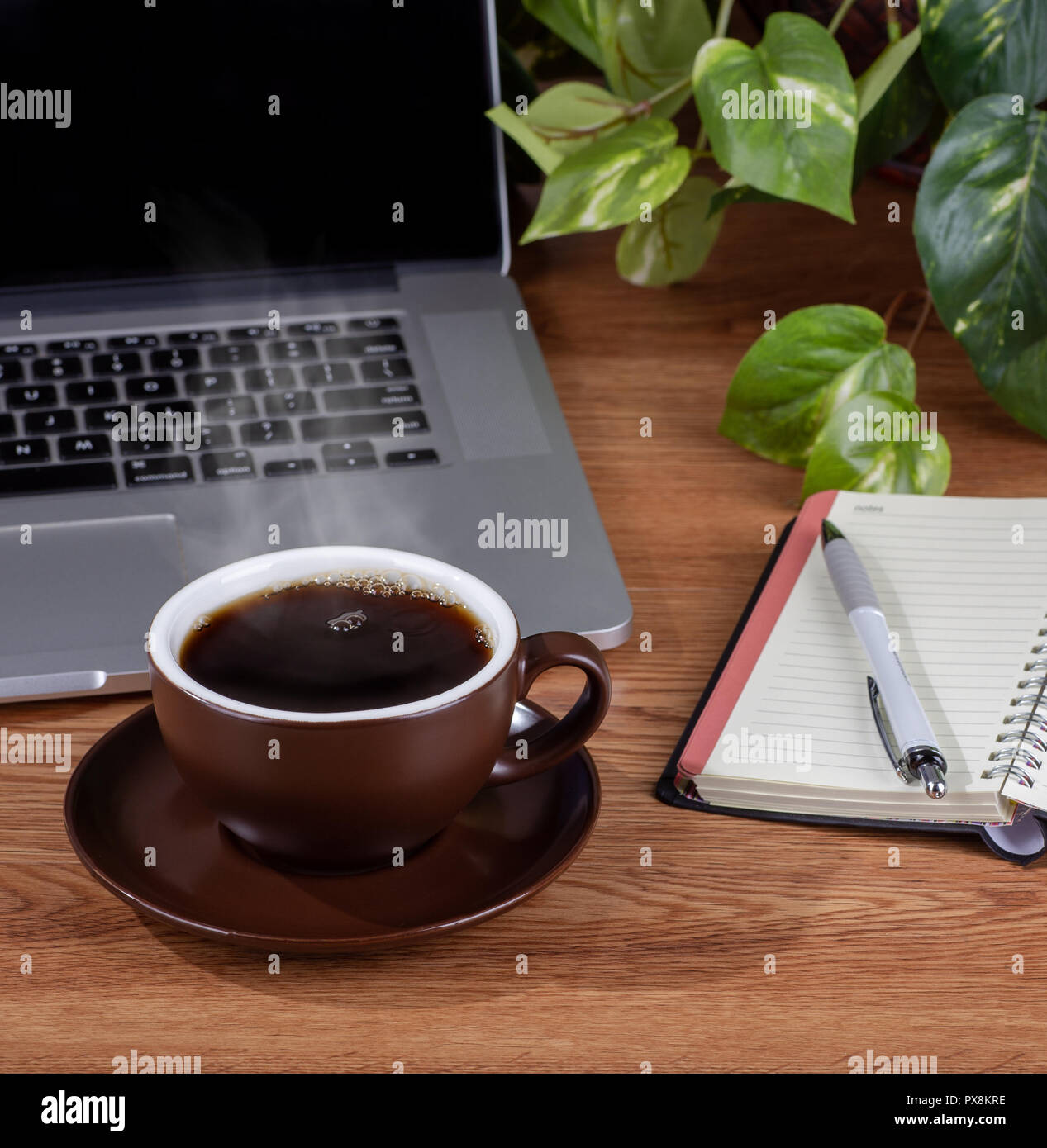 Cup of coffee with steam on a wooden desktop with a notebook and laptop ...