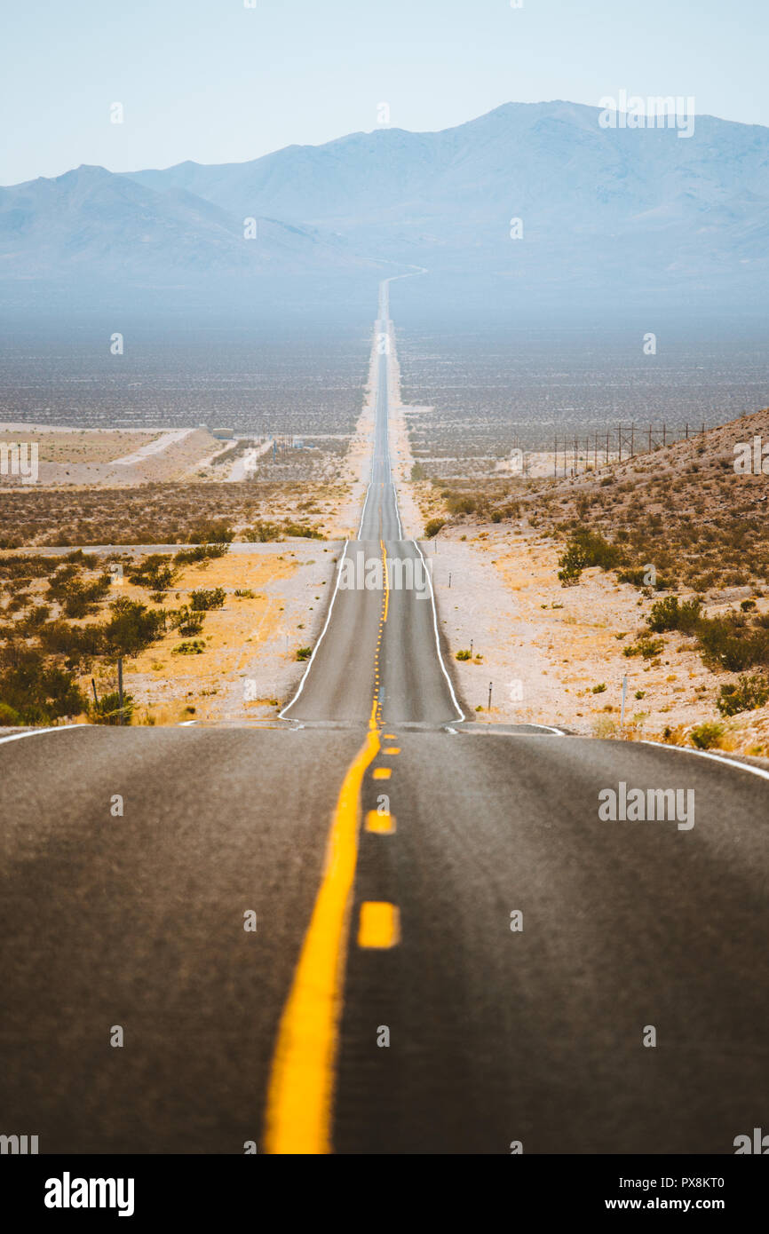 Classic panorama view of an endless straight road running through the barren scenery of the American Southwest with heat haze in summer Stock Photo