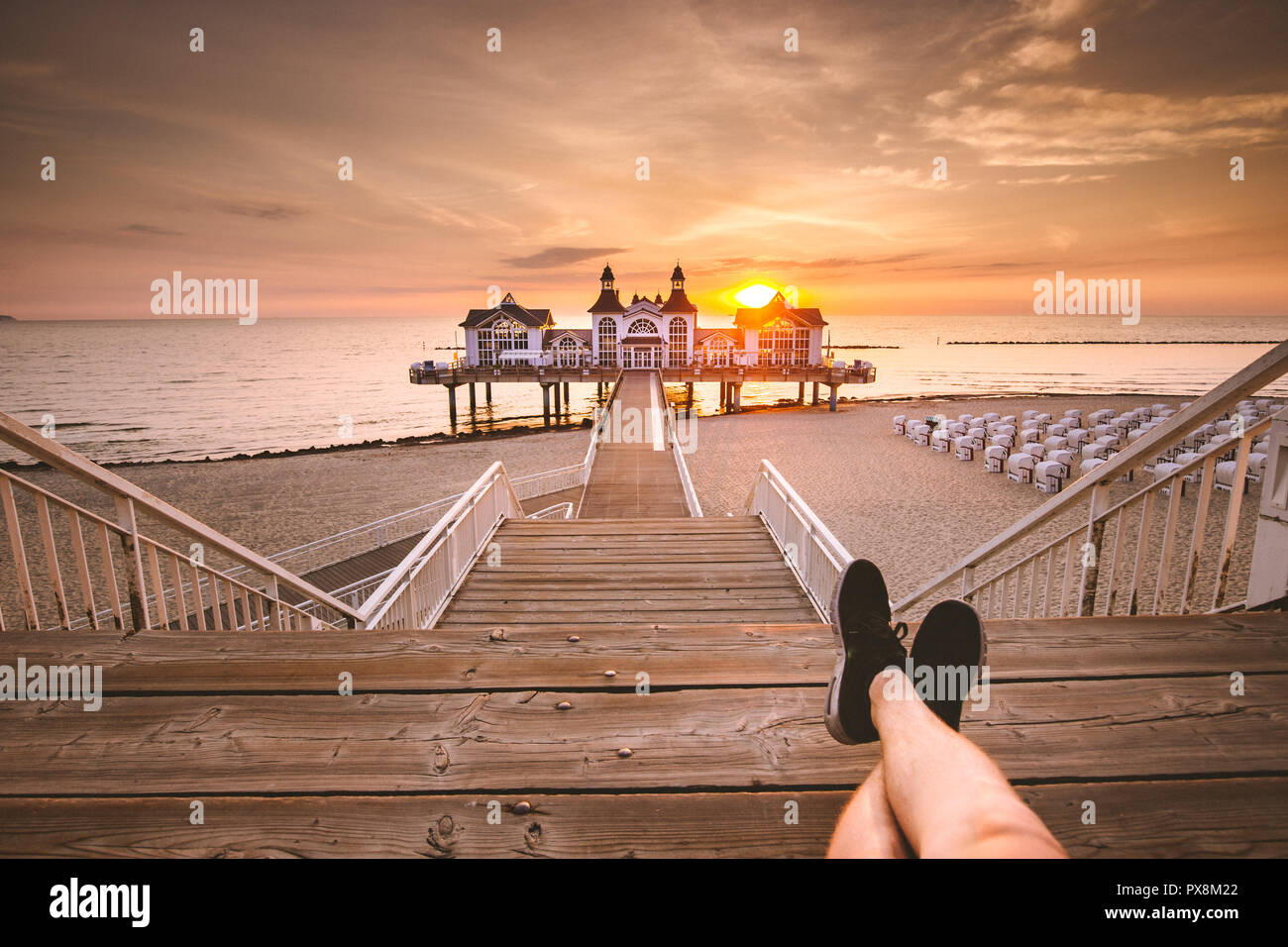 Young man sitting on wooden pier enjoying beautiful sunrise at famous Seebrucke Sellin at Ostseebad Sellin, island of Ruegen, Baltic Sea, Germany Stock Photo