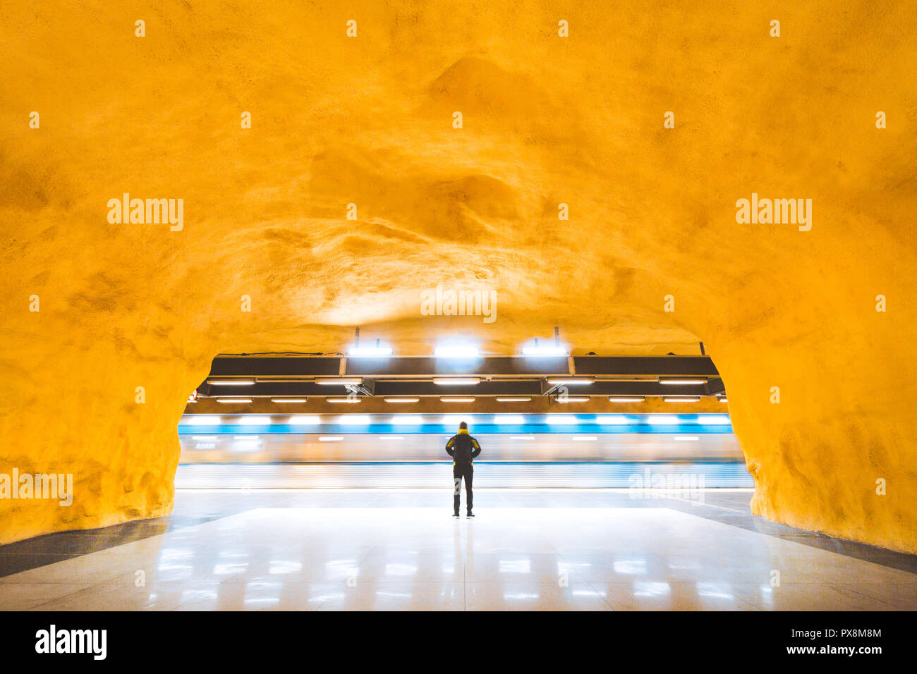 Panorama view of young male commuter standing in subway station watching trains pass by during rush hour, Stockholm, Sweden Stock Photo