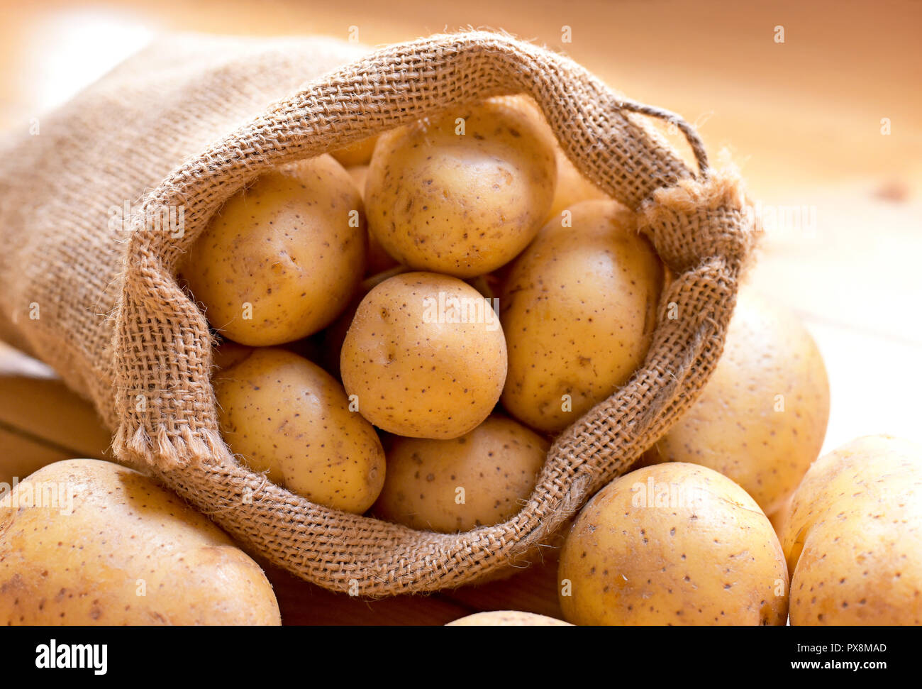 Fresh raw potatoes in a burlap sack. Earthy potato scene with sackcloth, arrangement on a wooden background, cooking ingredient. Stock Photo