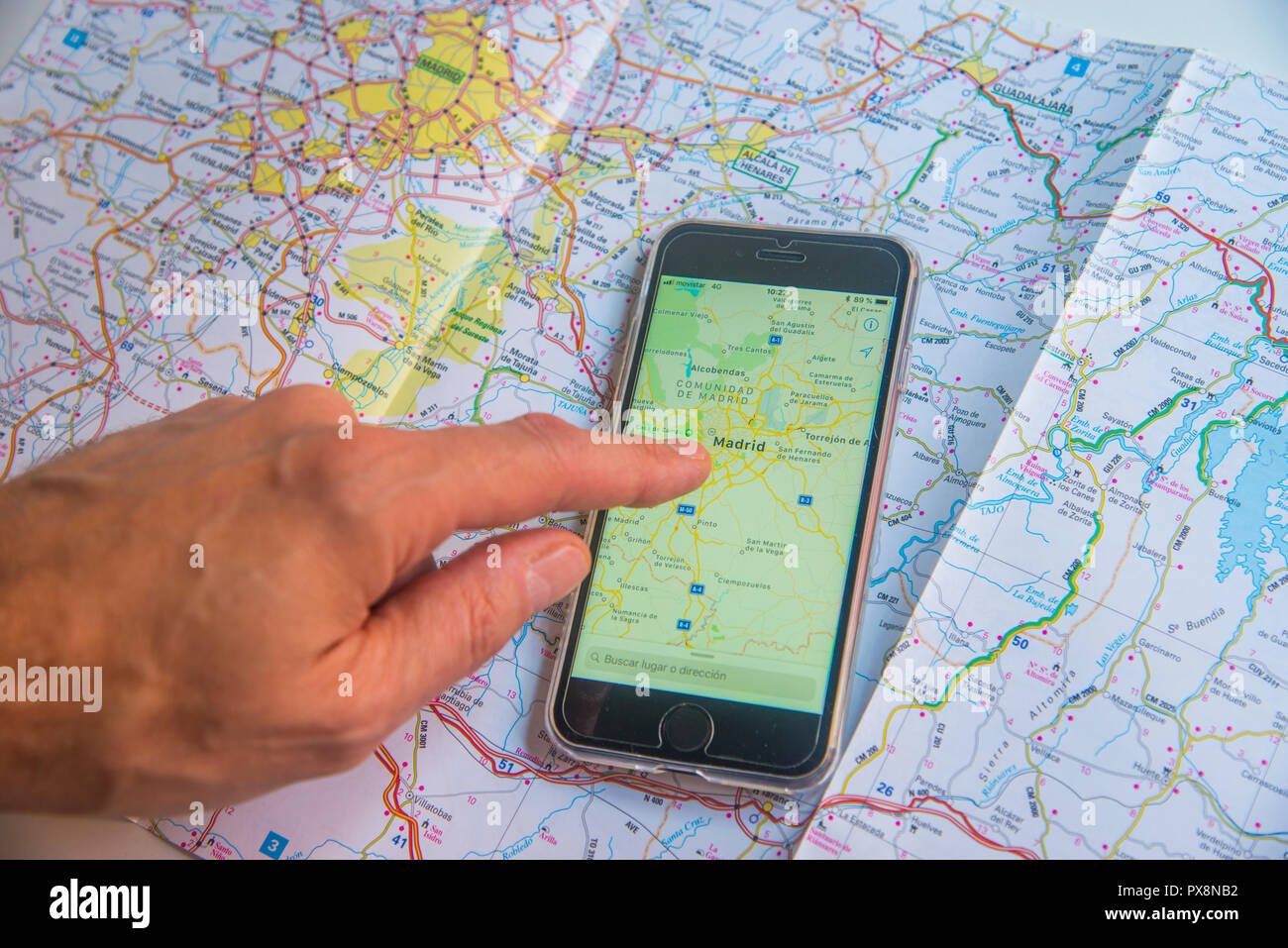 Hand pointing Madrid in the screen of a smartphone placed on a road map showing the same map. Stock Photo