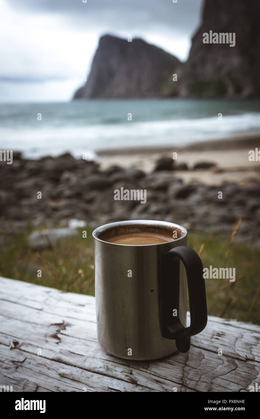 coffee cup on a rock at the sea in front of mountains and waves