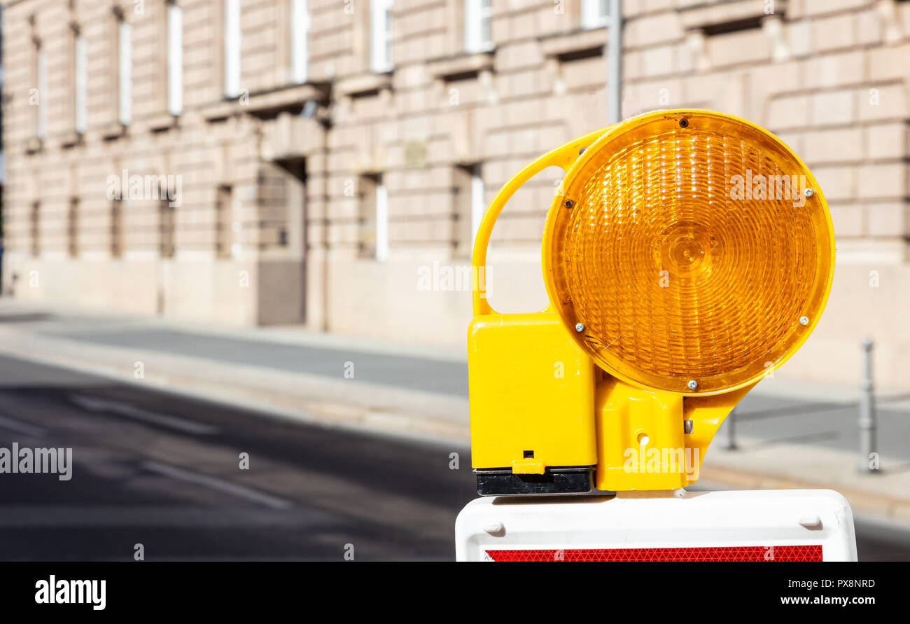 Construction site and safety. Street barricade with warning signal lamp on a road, blur building background Stock Photo