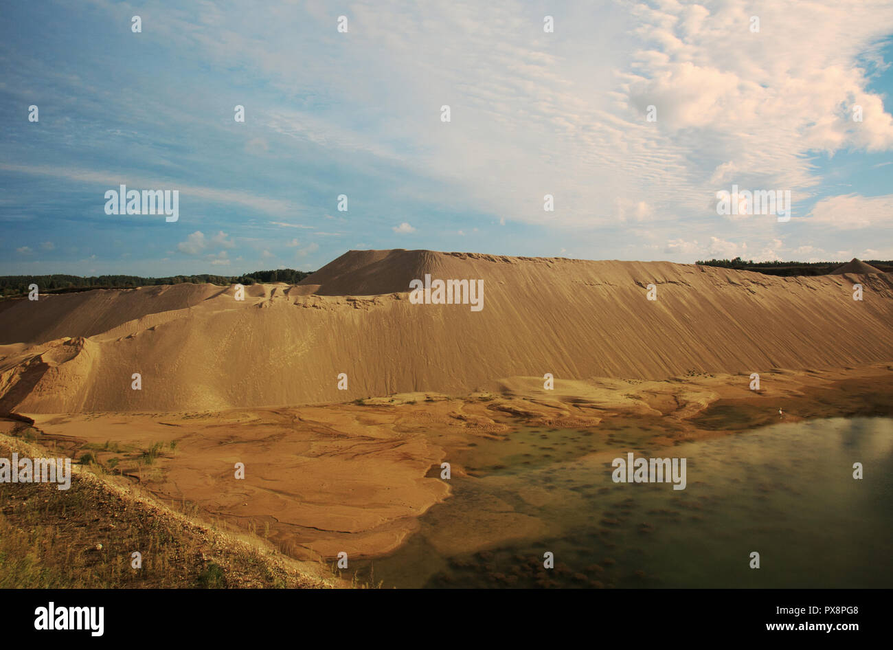 The view of the heaps of sand and pond was created after gravel pitting, against a background of blue sky with delicate, white clouds. Wide, horizonta Stock Photo