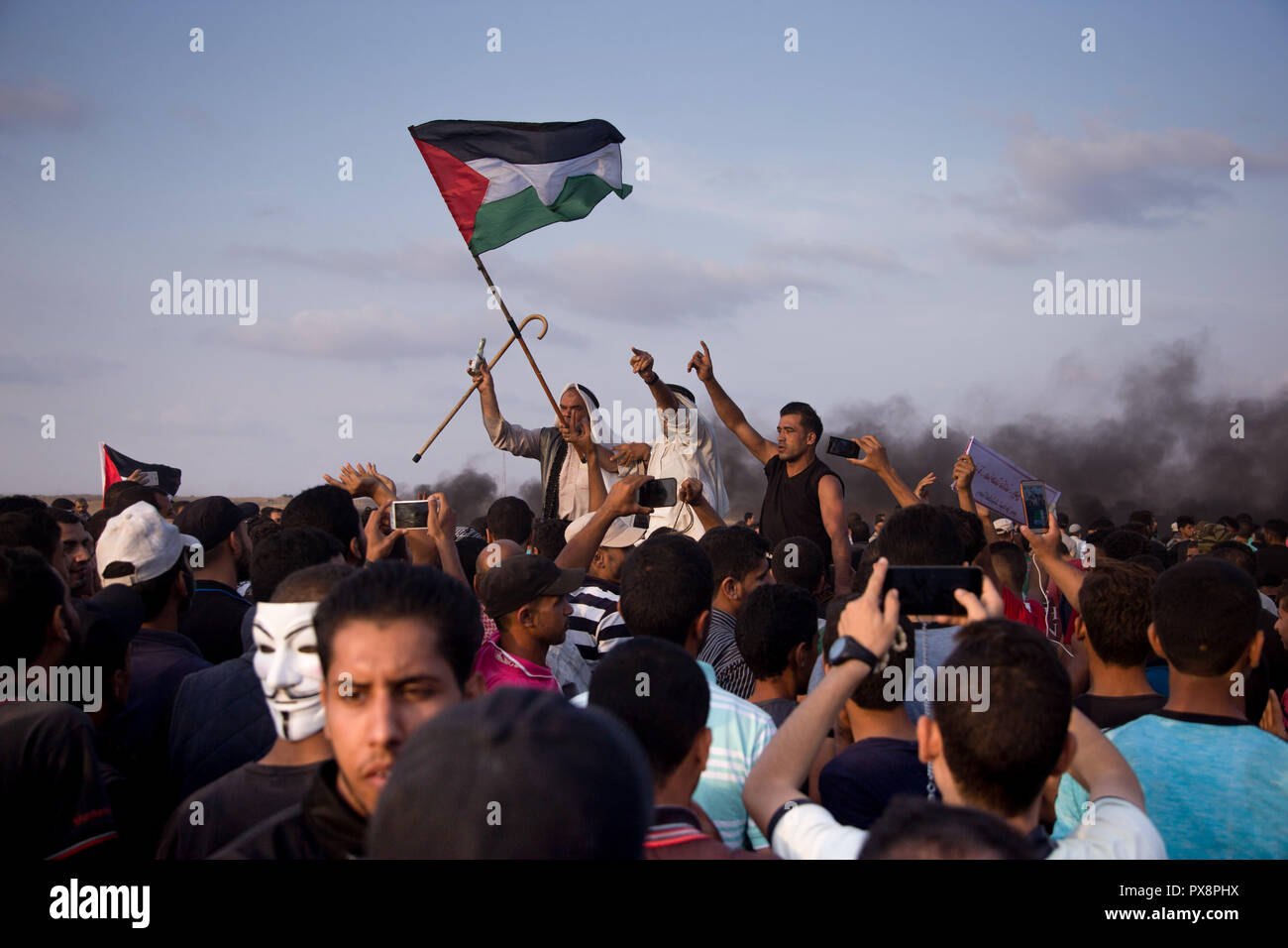 Palestinian demonstrators raise the flag of Palestine during the protest. Palestinians clash with Israeli forces during a protest calling for lifting the Israeli blockade on Gaza and demanding the right to return to their homeland, at the Israel-Gaza border fence in the southern Gaza Strip. Stock Photo
