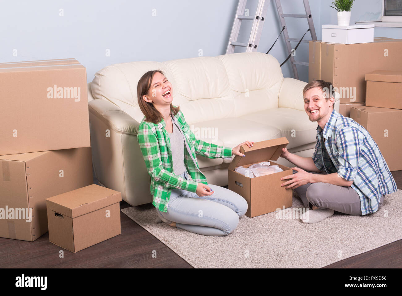 Moving and real estate concept - happy couple having fun unpacking ...