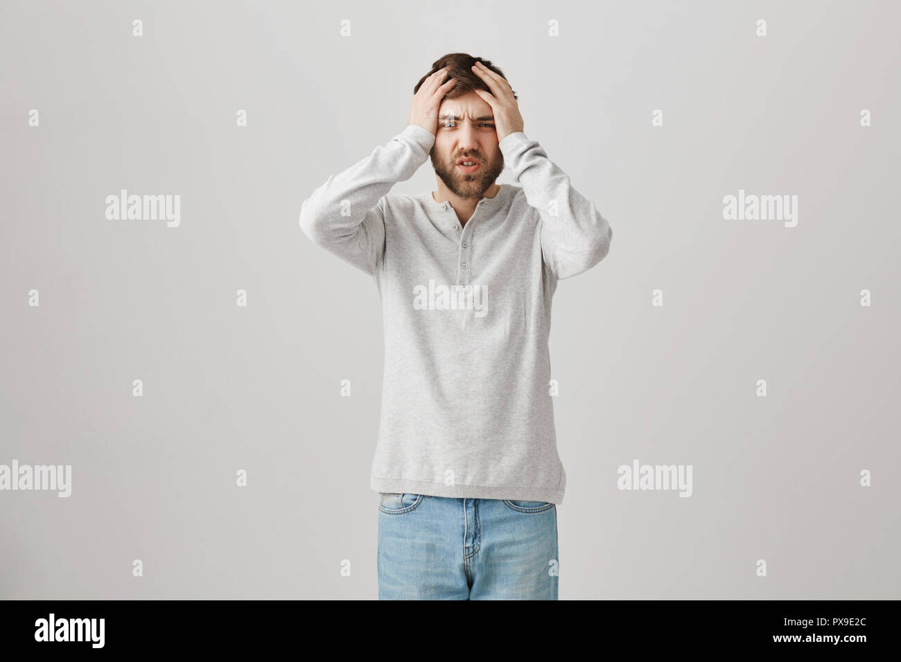 Man got into huge trouble. Studio shot of bothered and upset caucasian man holding head and frowning, losing all his money in casino, being devastated and troubled over gray background Stock Photo