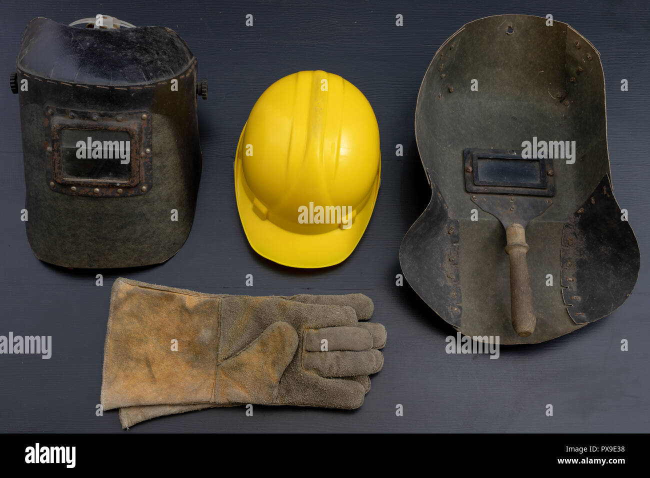 Welder's mask and gloves on a black workshop table. Protective clothing for workers in metalware. Dark background. Stock Photo