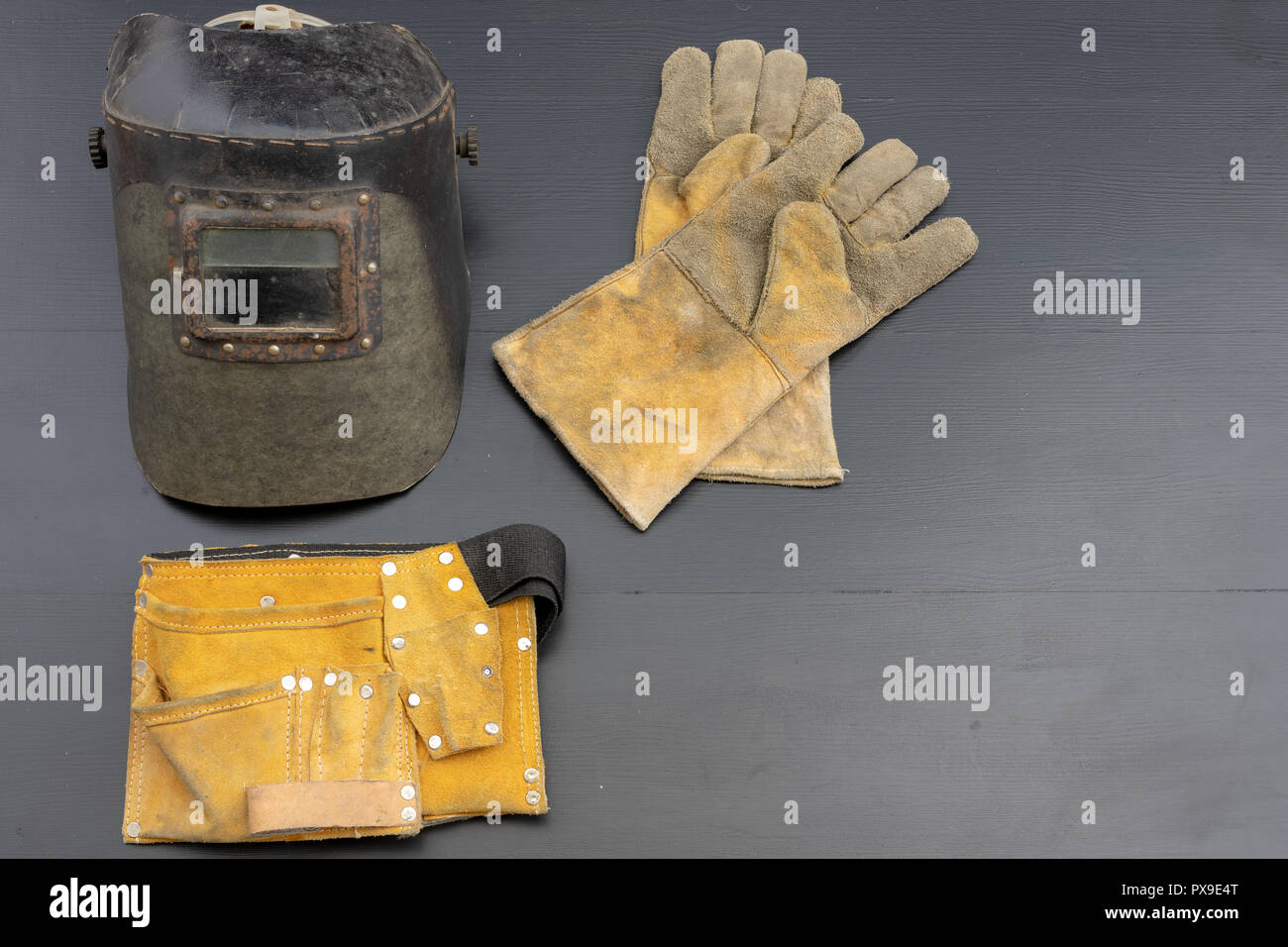 Welder's mask and gloves on a black workshop table. Protective clothing for workers in metalware. Dark background. Stock Photo