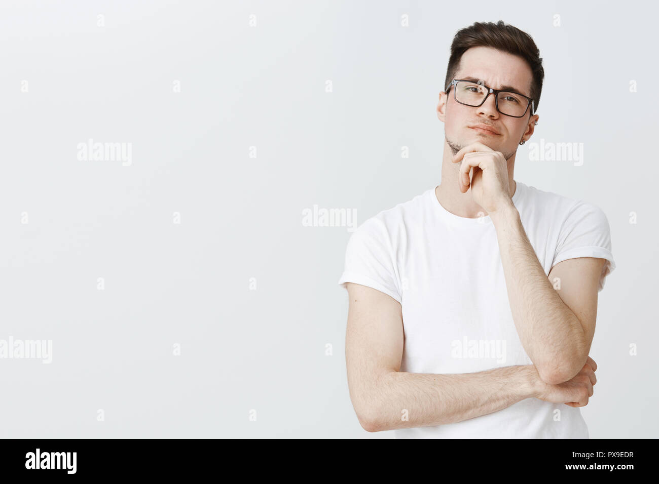 Waist-up shot of creative male photographer looking at model thoughtful holding hand on chin as thinkings making decision standing focused and serious standing against gray background determined Stock Photo