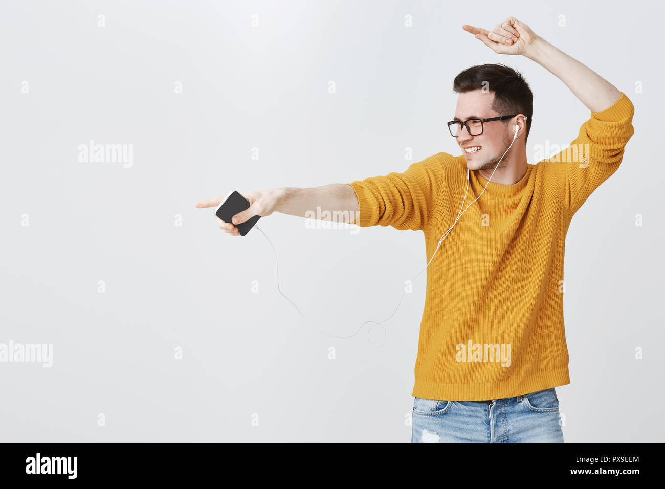Guy rocking dance-floor as listening music in earphones, dancing and  pointing left at copy space feeling enthusiastic and upbeat of enjoying  cool songs in earbuds, holding smartphone, wearing sweater Stock Photo -