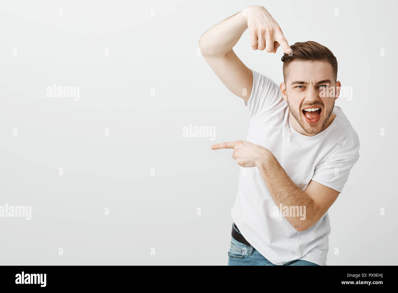 You go there. Portrait of stylish confident and emotive macho man with bristle and stylish haircut pointing at camera and left giving directions to move that way with daring cool expression Stock Photo