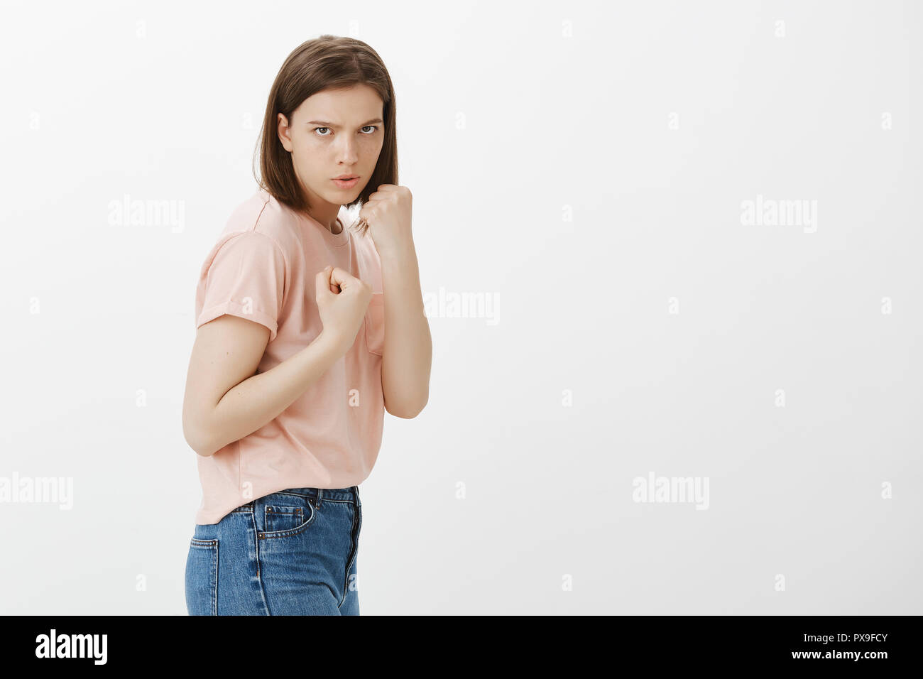 Wanna fight, bring it. Serious determined sportswoman in casual clothes, standing in fighter pose, holding fists clenched in boxer pose, defending herself, frowning and staring at camera Stock Photo