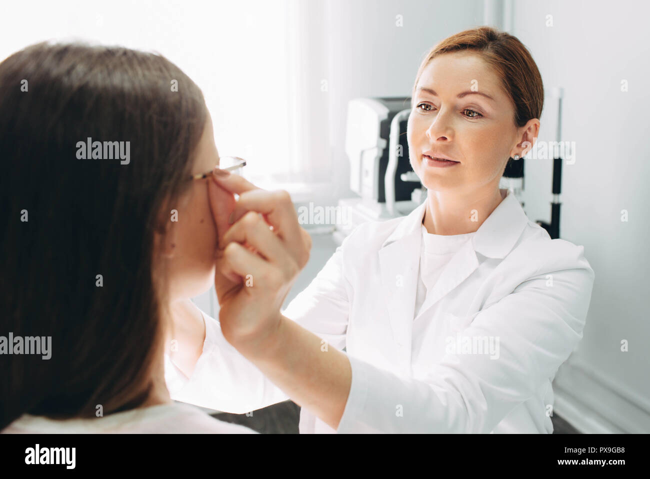 Optomerist is putting new glasses on girl face Stock Photo