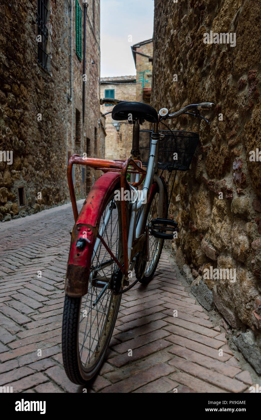 Red old bicycle with rust in a little alley of a medieval village Stock Photo