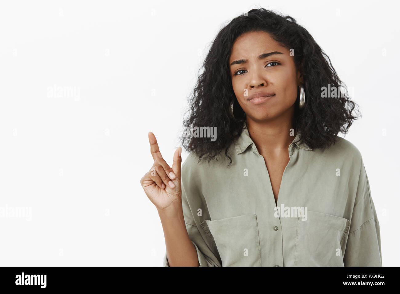 Size matters. Portrait of unimpressed displeased awkward cute african american woman in blouse smirking and chuckling shaping with hand small or tiny object posing over gray background Stock Photo