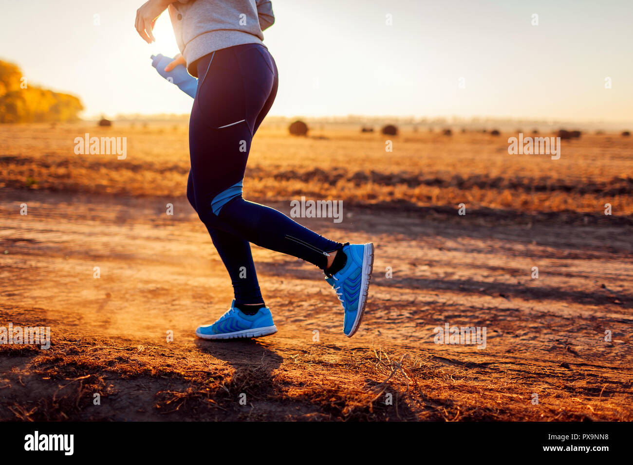 Woman running in autumn field at sunset. Healthy lifestyle concept. Active sportive people. Close up of legs Stock Photo