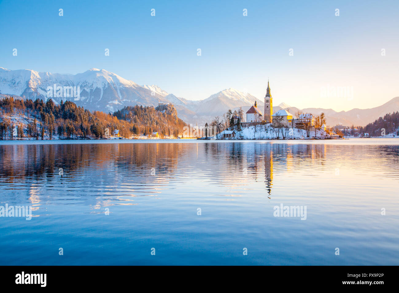 Beautiful view of famous Bled Island at scenic Lake Bled with Bled Castle and Julian Alps in the background in golden morning light at sunrise in wint Stock Photo