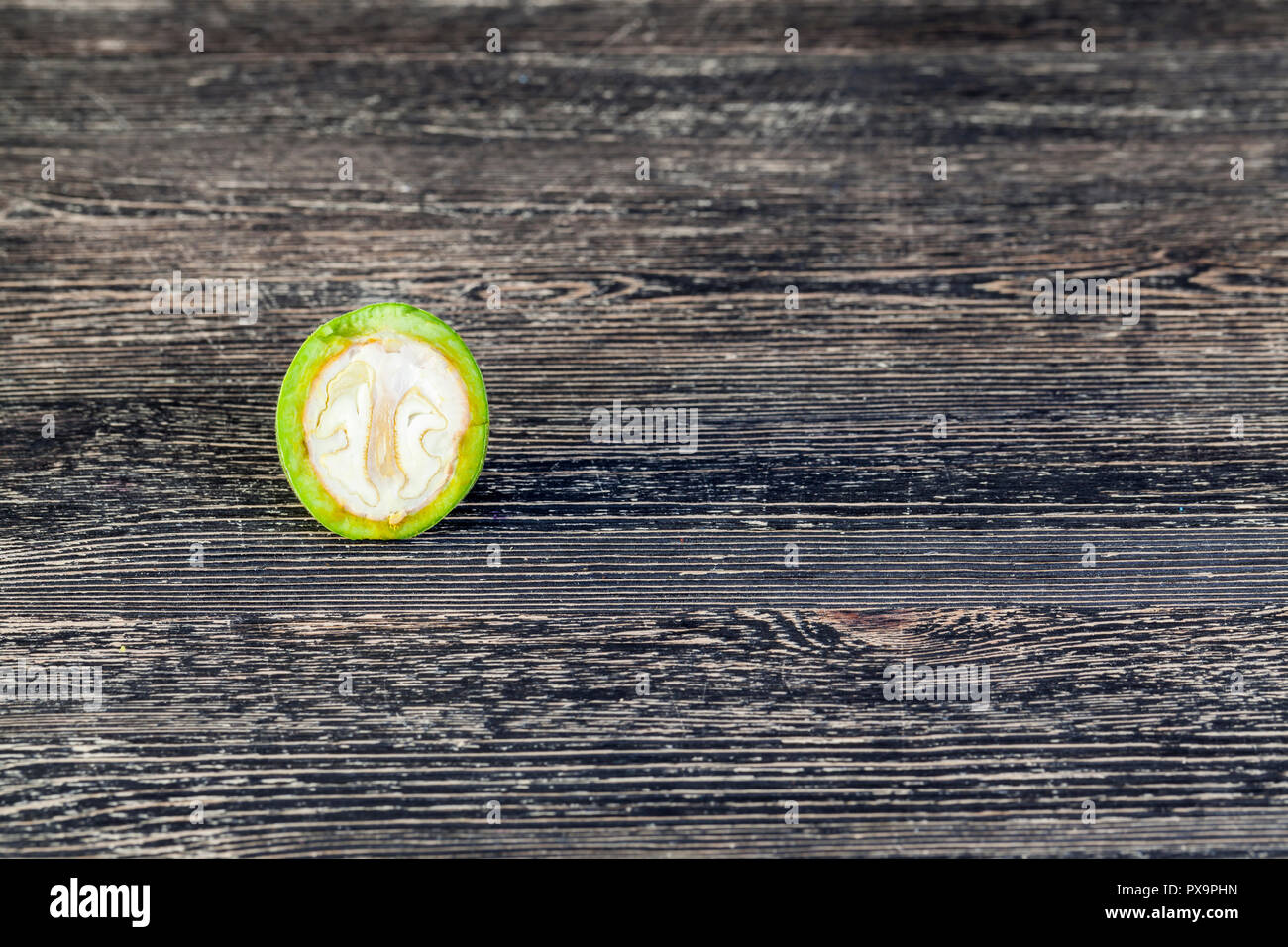 cut and broken piece of green walnut that is not ripe, on a black table Stock Photo