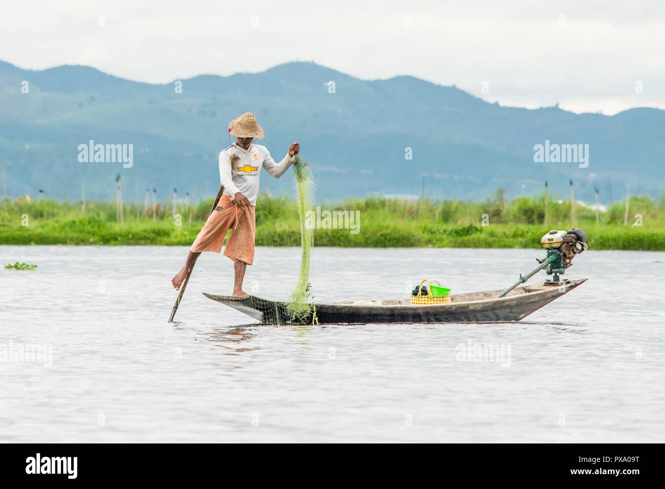 Travel: local young Burmese fisherman wearing Manchester United shirt, balancing and steering boat with his foot in Inle Lake, Burma, Myanmar, Asia Stock Photo