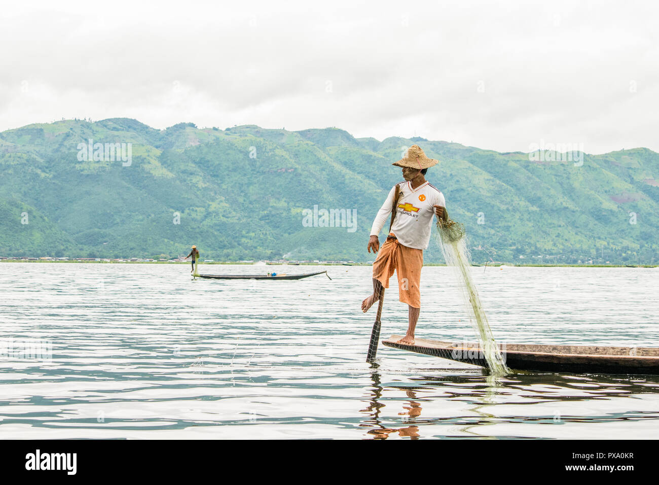 Travel: local young Burmese fisherman wearing Manchester United shirt, balancing and steering boat with his foot in Inle Lake, Burma, Myanmar, Asia Stock Photo
