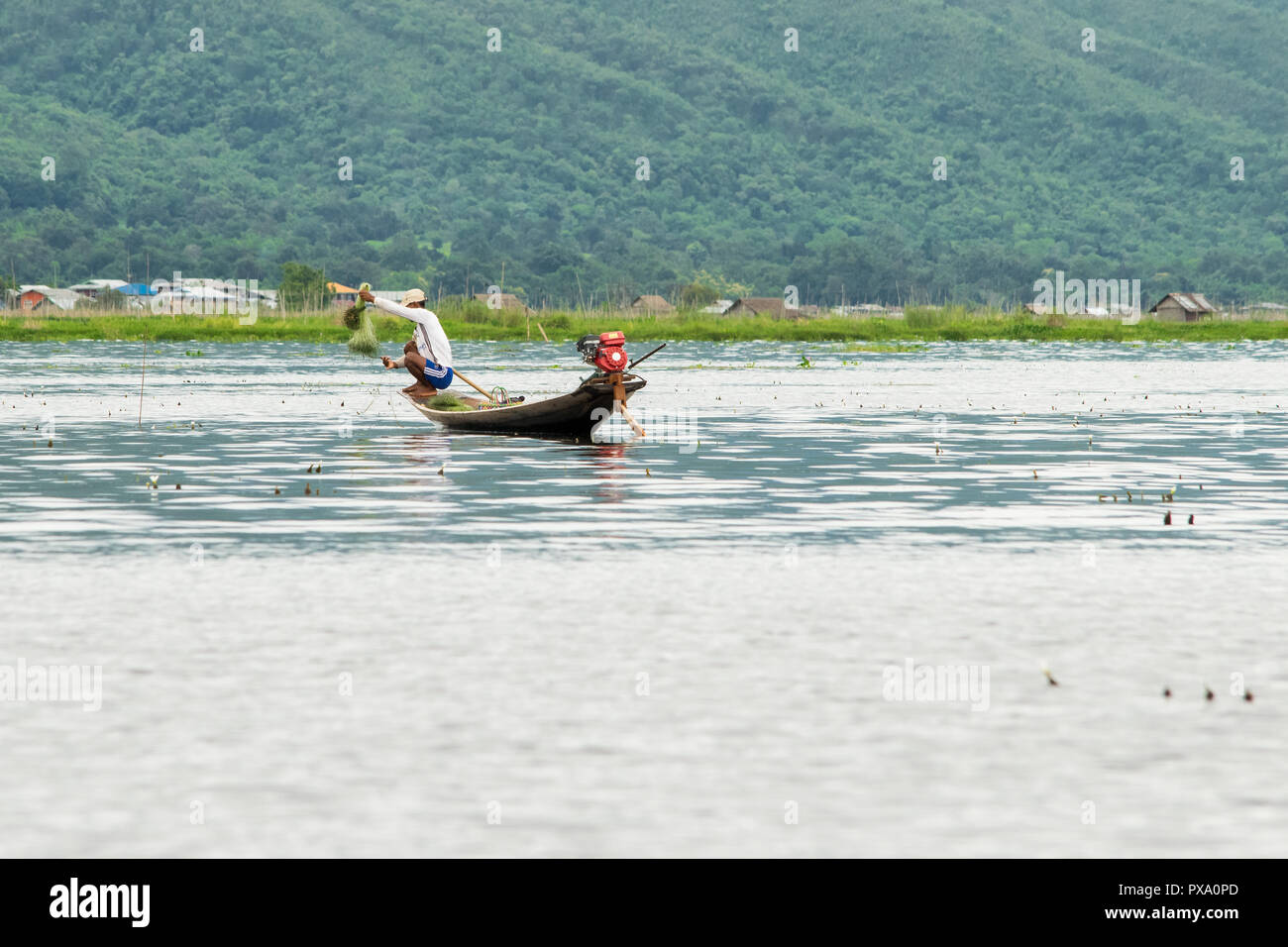 Young fisherman with net, crouching squat on a long boat, balancing. traditional boat and fishing techniques. Inle Lake, Shan region, Myanmar, Burma Stock Photo