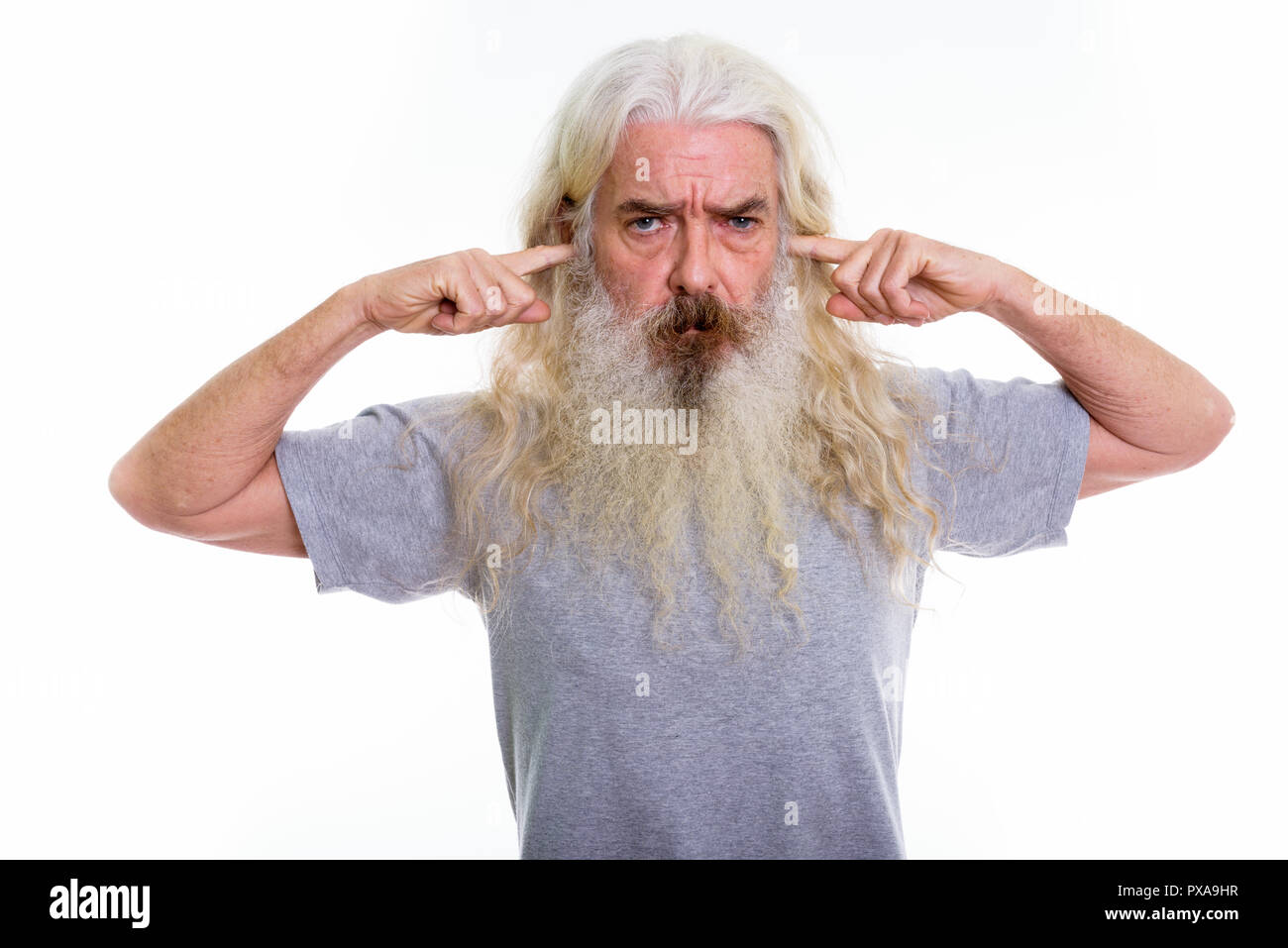 Studio shot of senior bearded man thinking while covering ears w Stock Photo